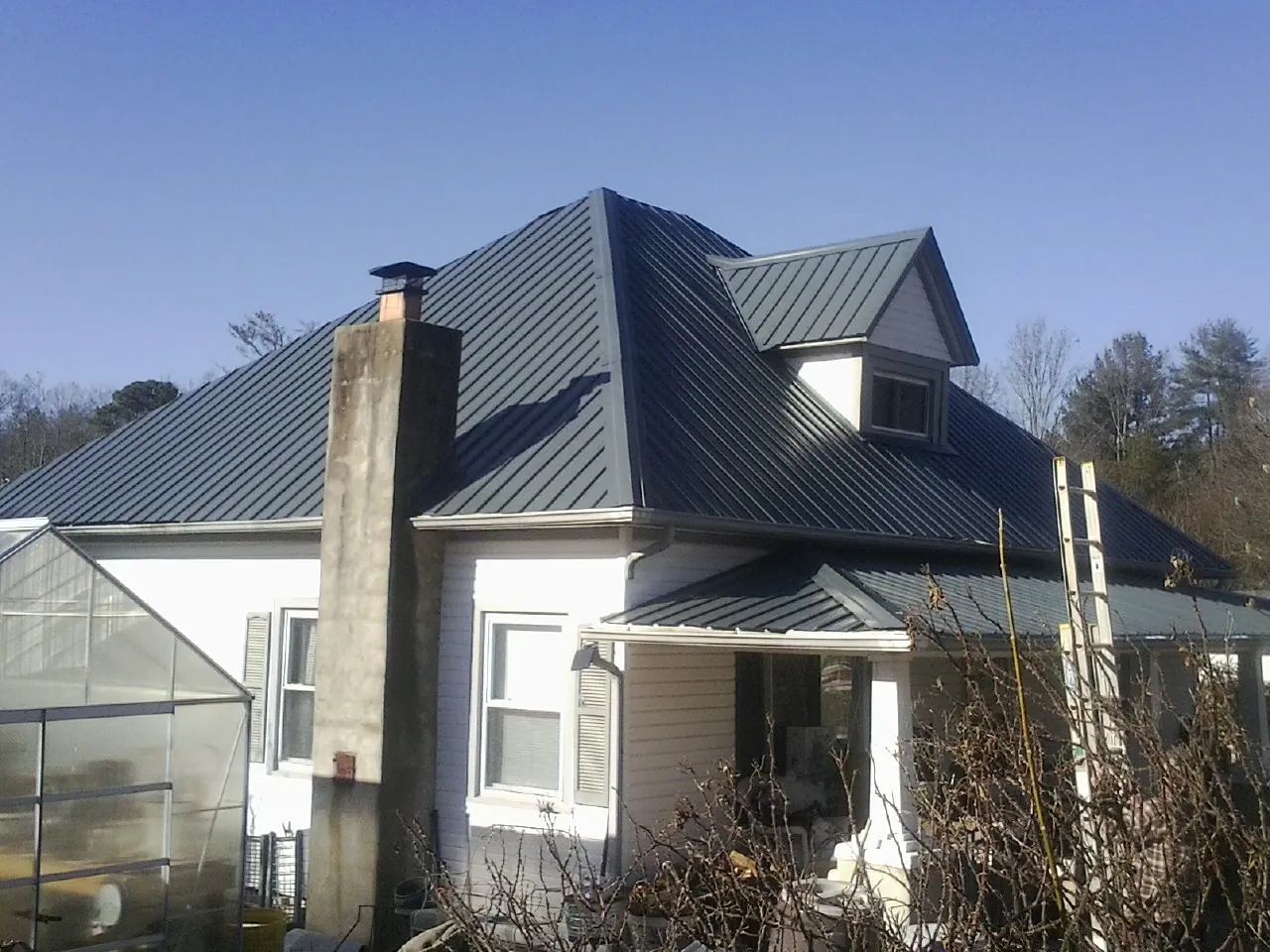 Dark blue standing seam metal roof on a white farmhouse with dormer — Slate & Tile Roof Repair by Roofing Brothers in East Rockaway