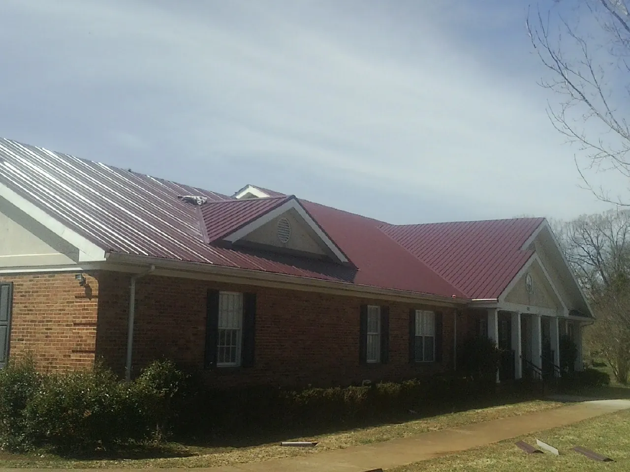 Red metal roof with gabled entries on a long brick building, from a Hail Damage Roof Repair job in East Rockaway