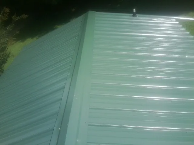New green metal panels meeting at the ridge of a roof — Flat Roof Repair work by our crew in East Rockaway