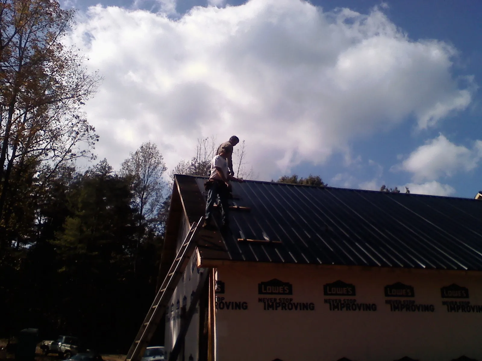 Roofer fastening dark metal panels high against a cloudy sky, from a Roof Inspection job in East Rockaway