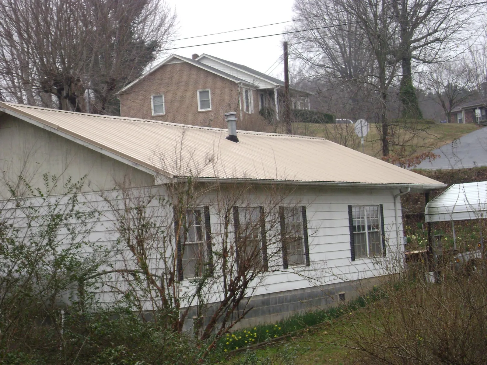 Tan metal roof on a white sided house set into a hillside — Commercial Roofing by Roofing Brothers in East Rockaway