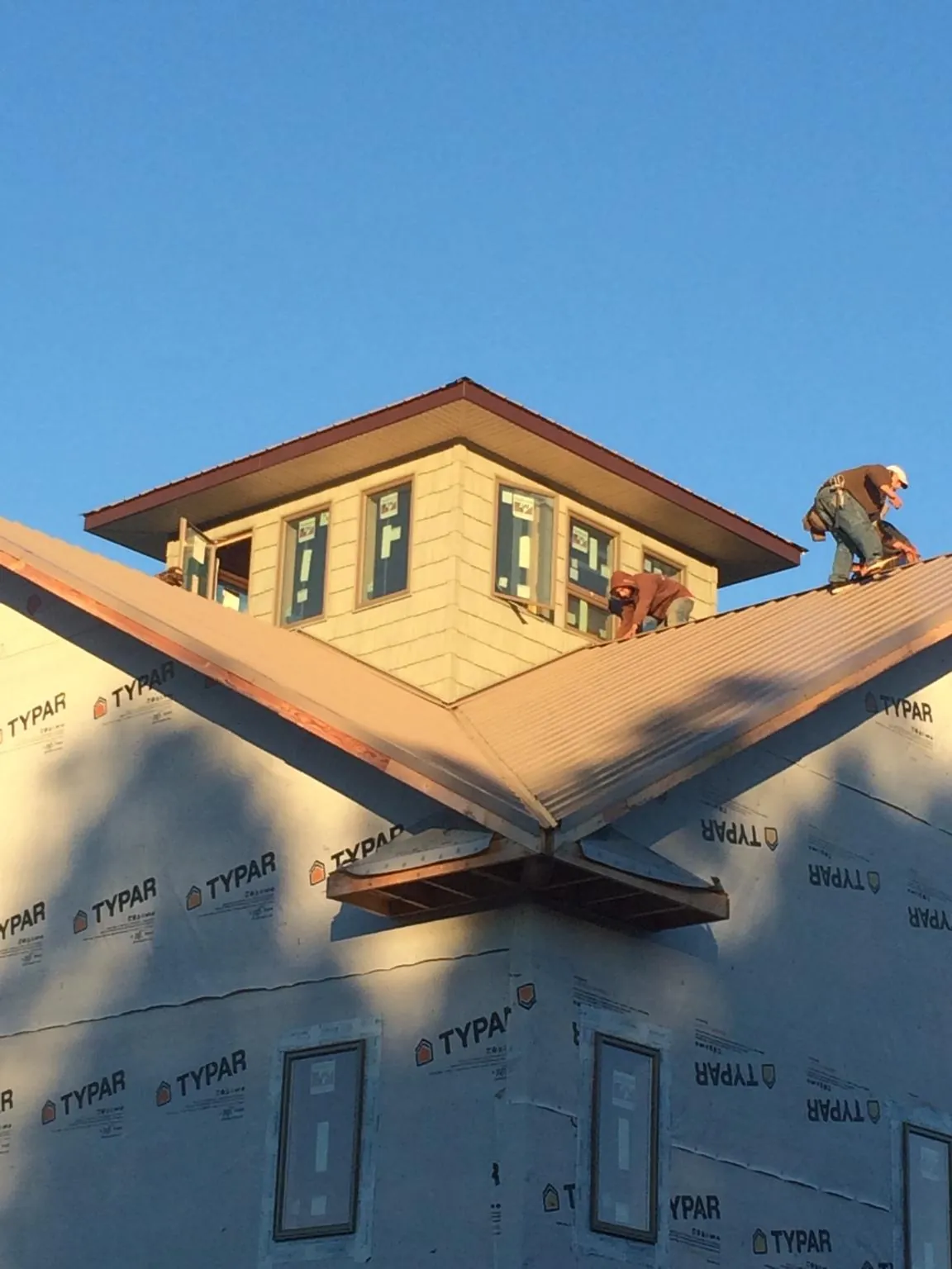 Roofers working around a rooftop cupola on a new metal roof at sunset in East Rockaway